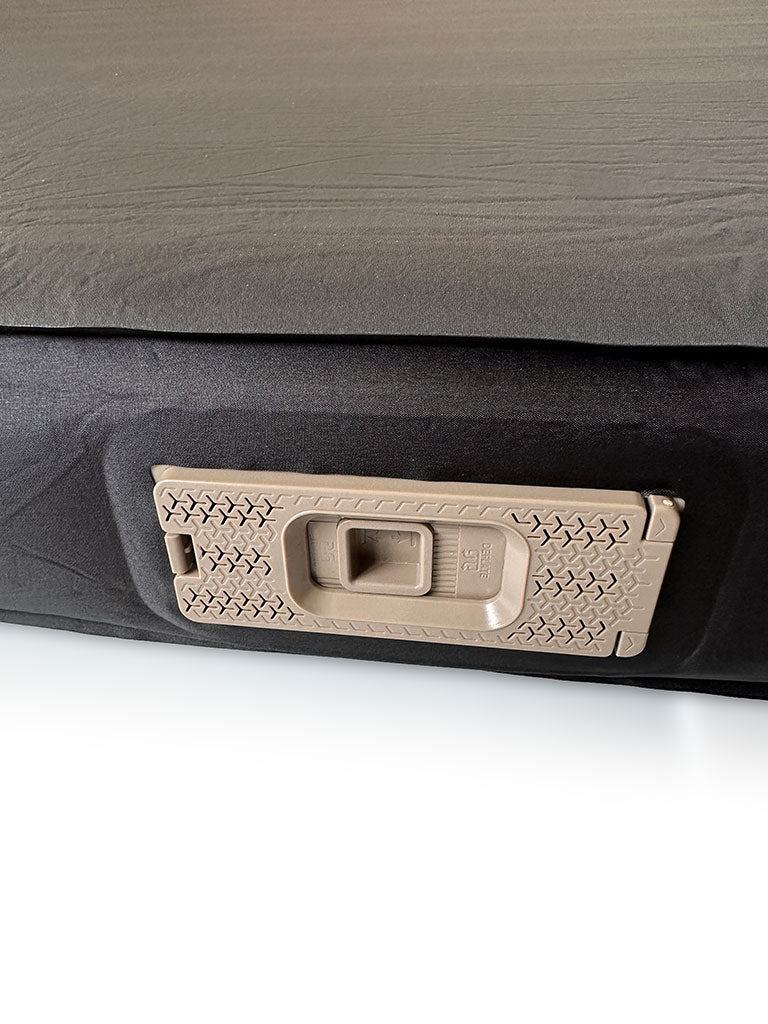 Close-up of the inflation pump on a Lucas Creek self-inflating mattress, showing a beige textured mechanism set into the black mattress fabric.